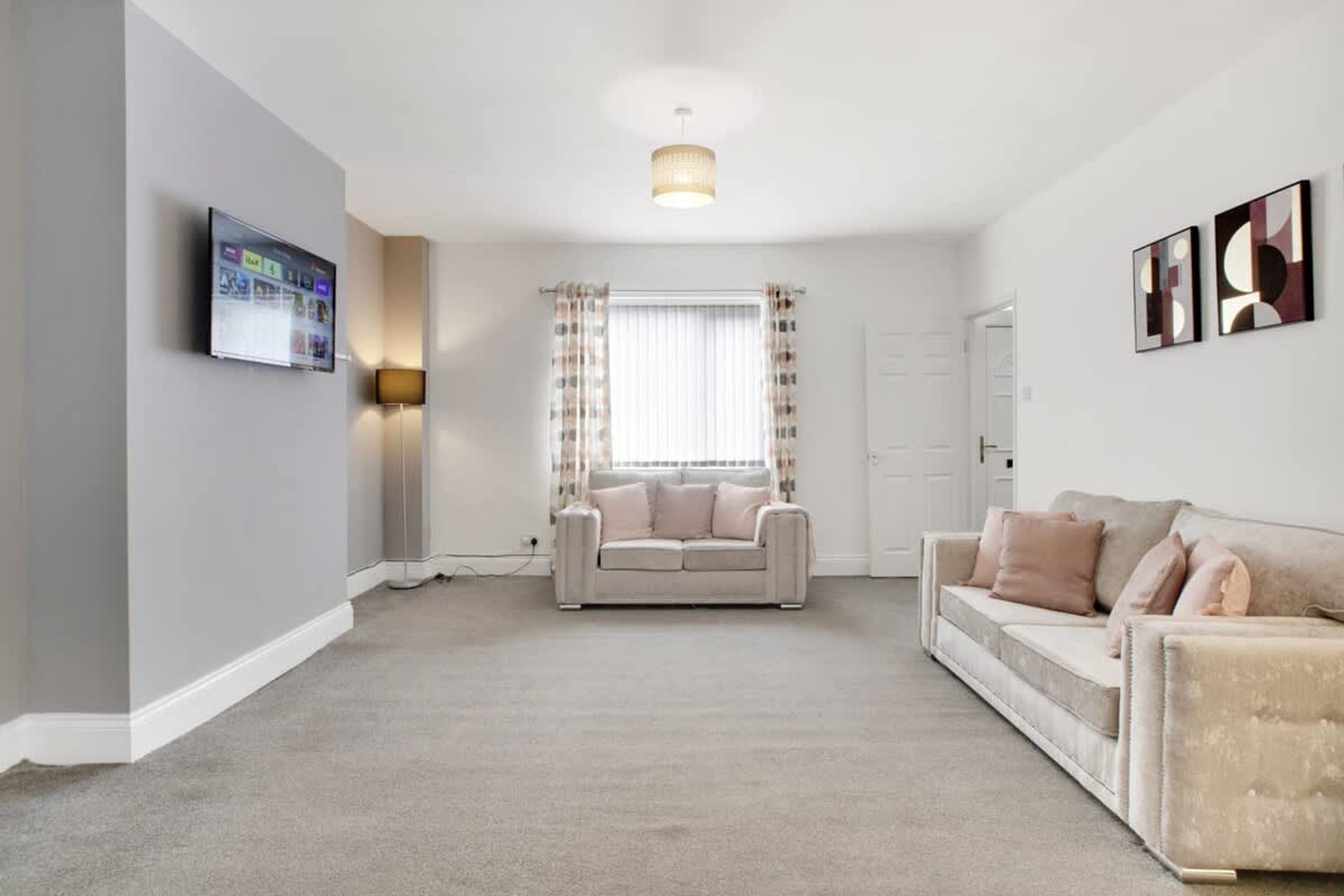 A spacious living room with a large window, a flat-screen TV mounted on the wall, and two sofas.