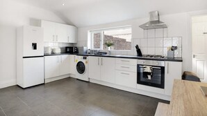 A modern kitchen with white cabinetry, a built-in washing machine, a gas stove, and a view of the city through a window. - Stylish 2BR House in Ashington by Stay With Us (Ashington)