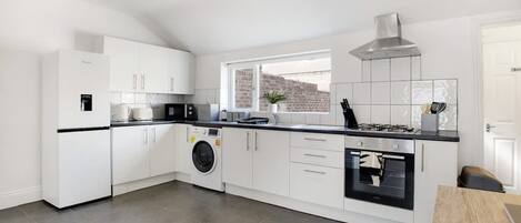 A modern kitchen with white cabinetry, a built-in washing machine, a gas stove, and a view of the city through a window.