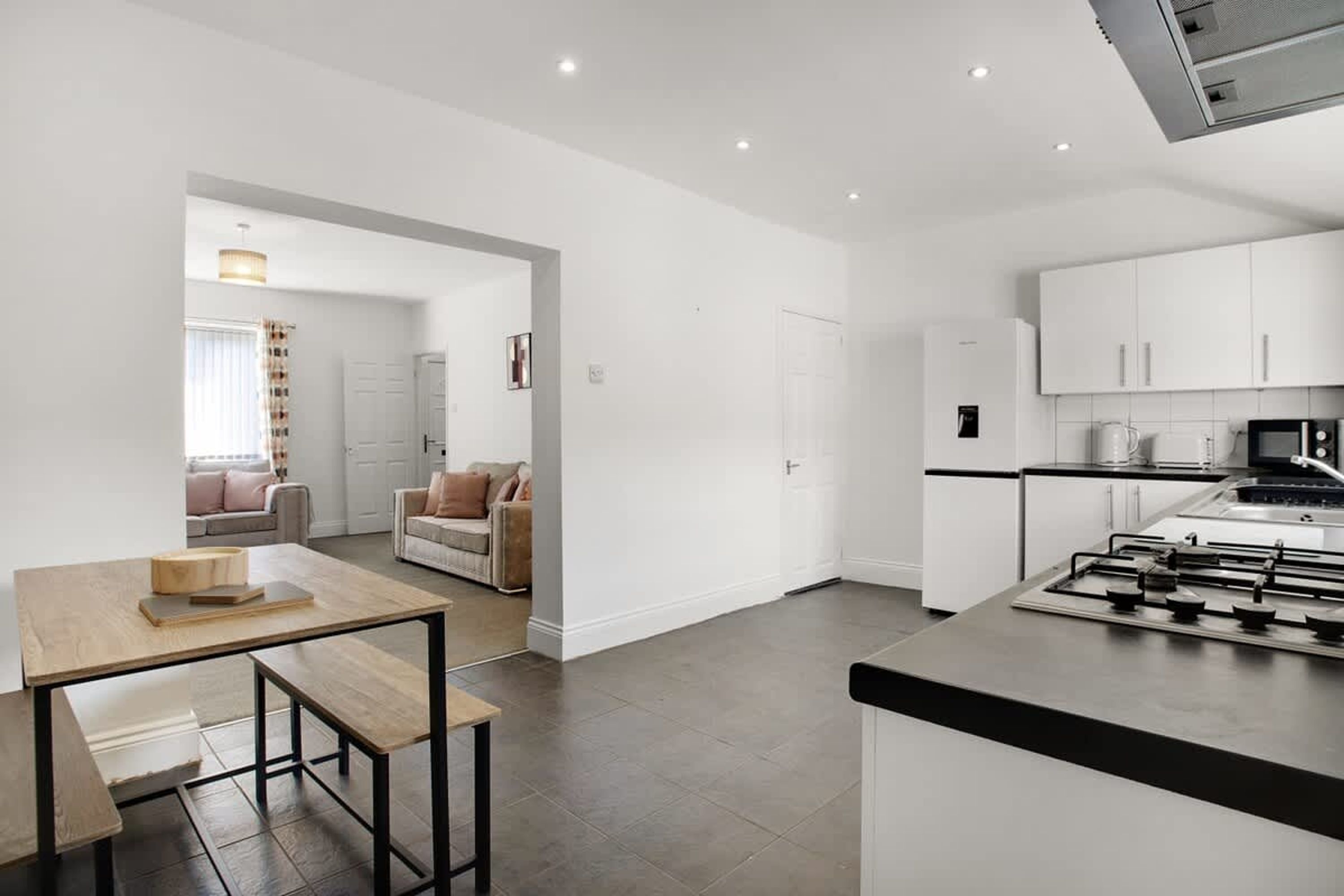 Una cocina moderna con una isla central, un comedor con mesa y bancos de madera, y una sala de estar con sofá y mesa de centro.