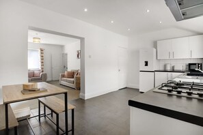 A modern kitchen with a central island, a dining area with a wooden table and benches, and a living room with a sofa and a coffee table. - Stylish 2BR House in Ashington by Stay With Us (Ashington)
