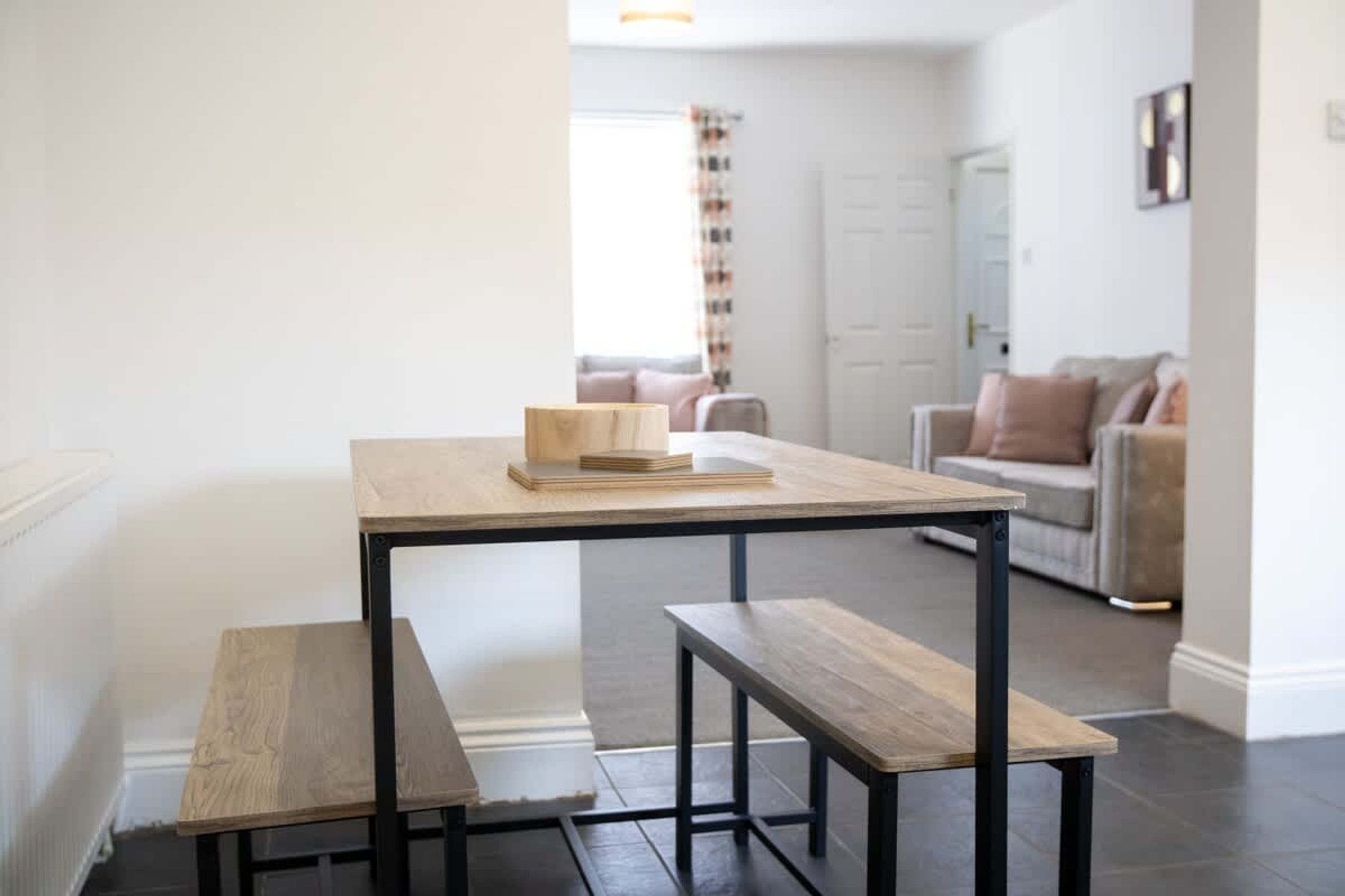 A minimalist living space with a wooden table and benches, a sofa, and a door in the background.