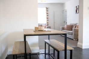 A minimalist living space with a wooden table and benches, a sofa, and a door in the background. - Stylish 2BR House in Ashington by Stay With Us (Ashington)