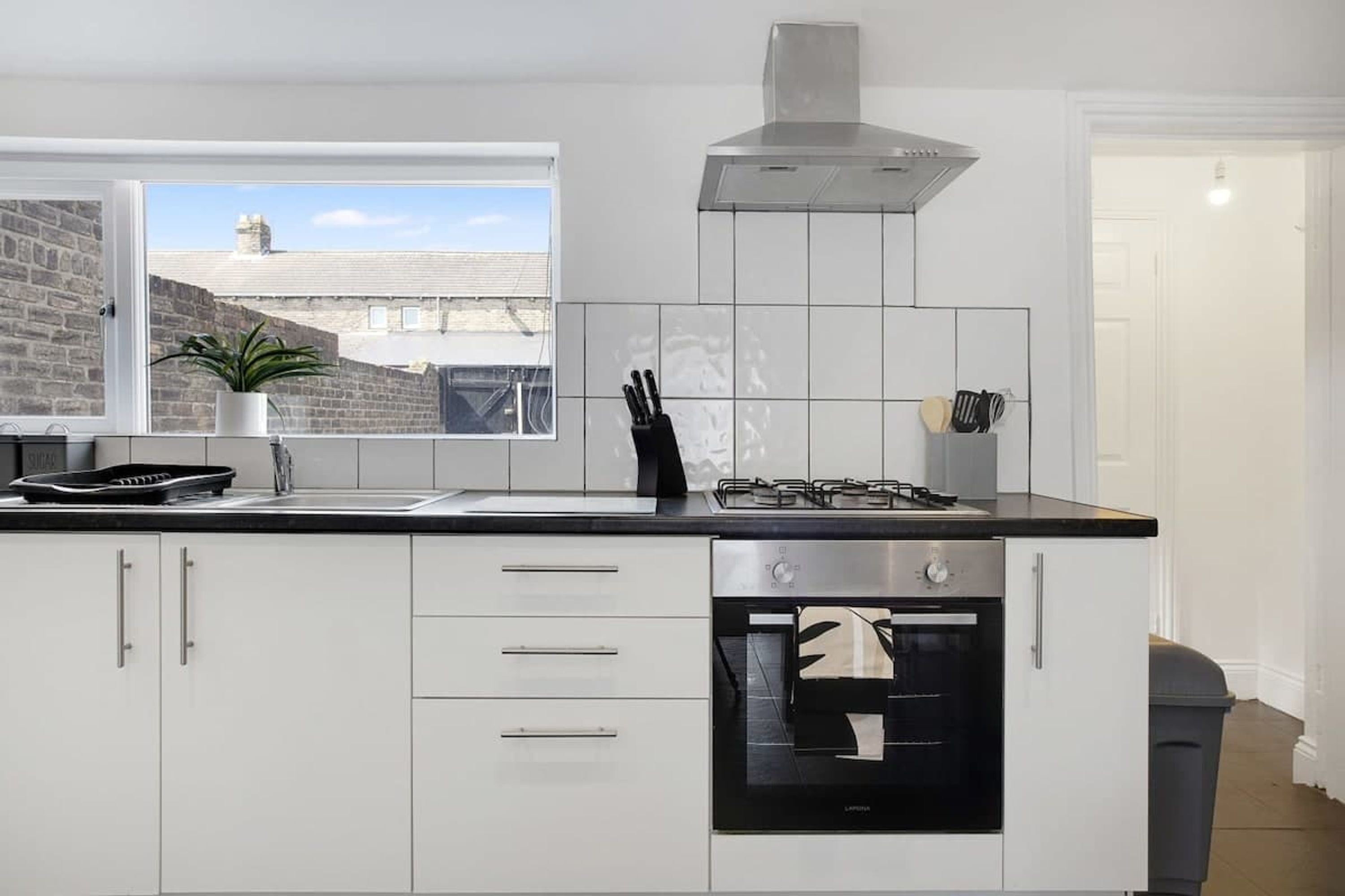 A modern kitchen with white cabinetry, a gas stove, a built-in oven, and a window with a view of a brick building.