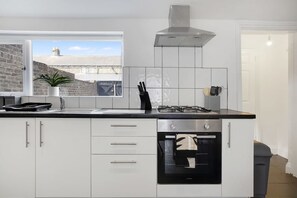 A modern kitchen with white cabinetry, a gas stove, a built-in oven, and a window with a view of a brick building. - Stylish 2BR House in Ashington by Stay With Us (Ashington)