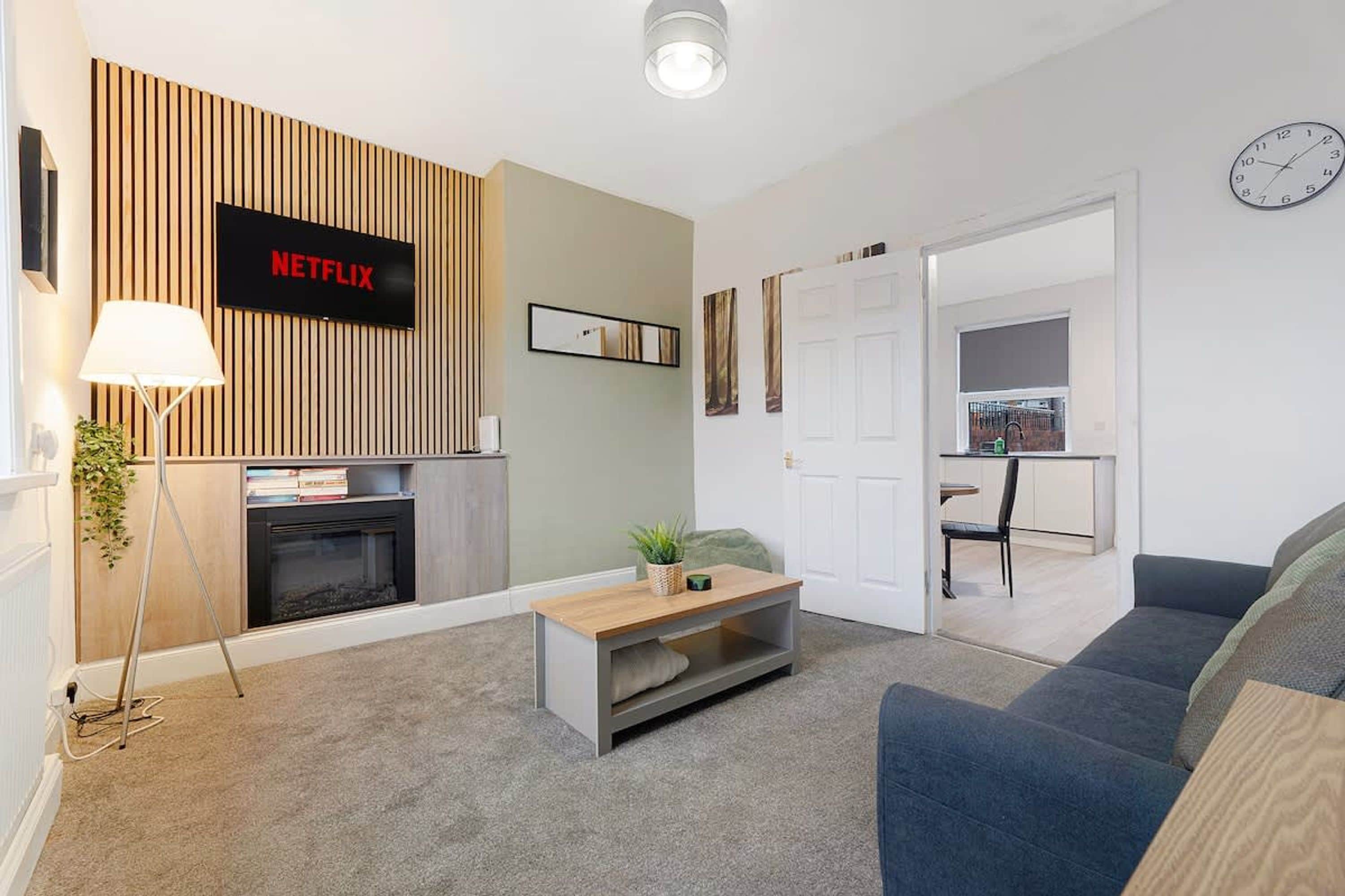 Un salon moderne avec une cheminée, un logo Netflix, un canapé, une table basse et, au fond, un coin repas.