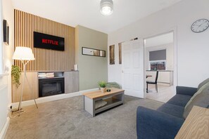 A modern living room with a fireplace, a Netflix sign, a sofa, a coffee table, and a dining area in the background. - Cosy 2BR Apartment Sleeps 4 by Stay With Us (Peterlee)
