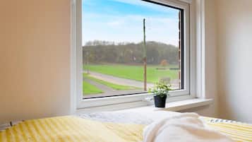 Una habitación con una cama, una ventana que da a un campo verde y una planta en maceta en el alféizar.