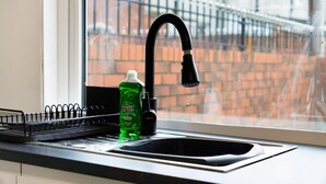 A kitchen sink with a black faucet and a bottle of green liquid soap. - Cosy 2BR Apartment Sleeps 4 by Stay With Us (Peterlee)
