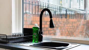 Un lavamanos de cocina con un grifo negro y una botella de jabón líquido verde.