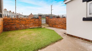 A residential property with a brick wall, a small grassy yard, and a white building. - Cosy 2BR Apartment Sleeps 4 by Stay With Us (Peterlee)