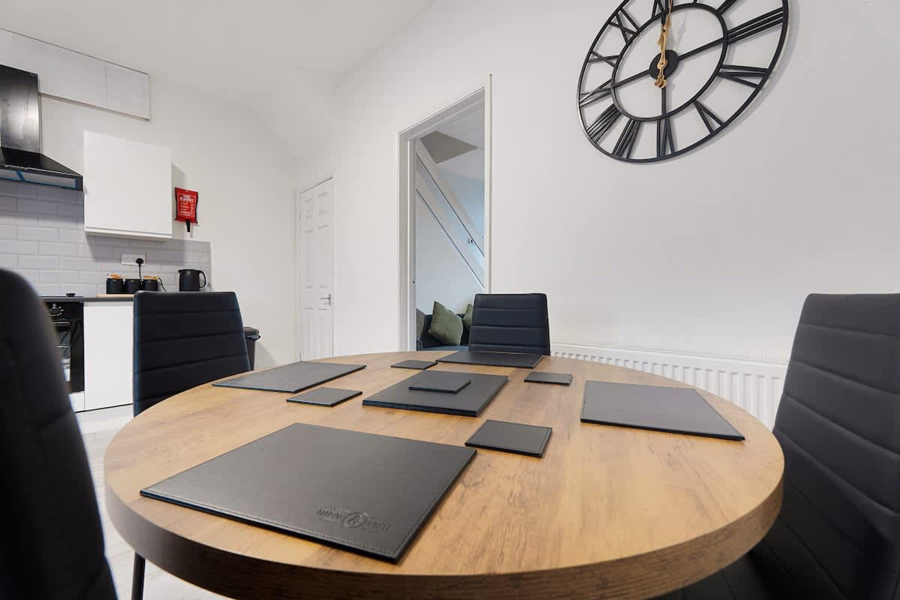 Un comedor moderno con una mesa redonda de madera, sillas negras y un gran reloj de pared.