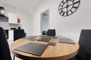 A modern dining room with a round wooden table, black chairs, and a large wall clock. - Cosy 2BR Apartment Sleeps 4 by Stay With Us (Peterlee)