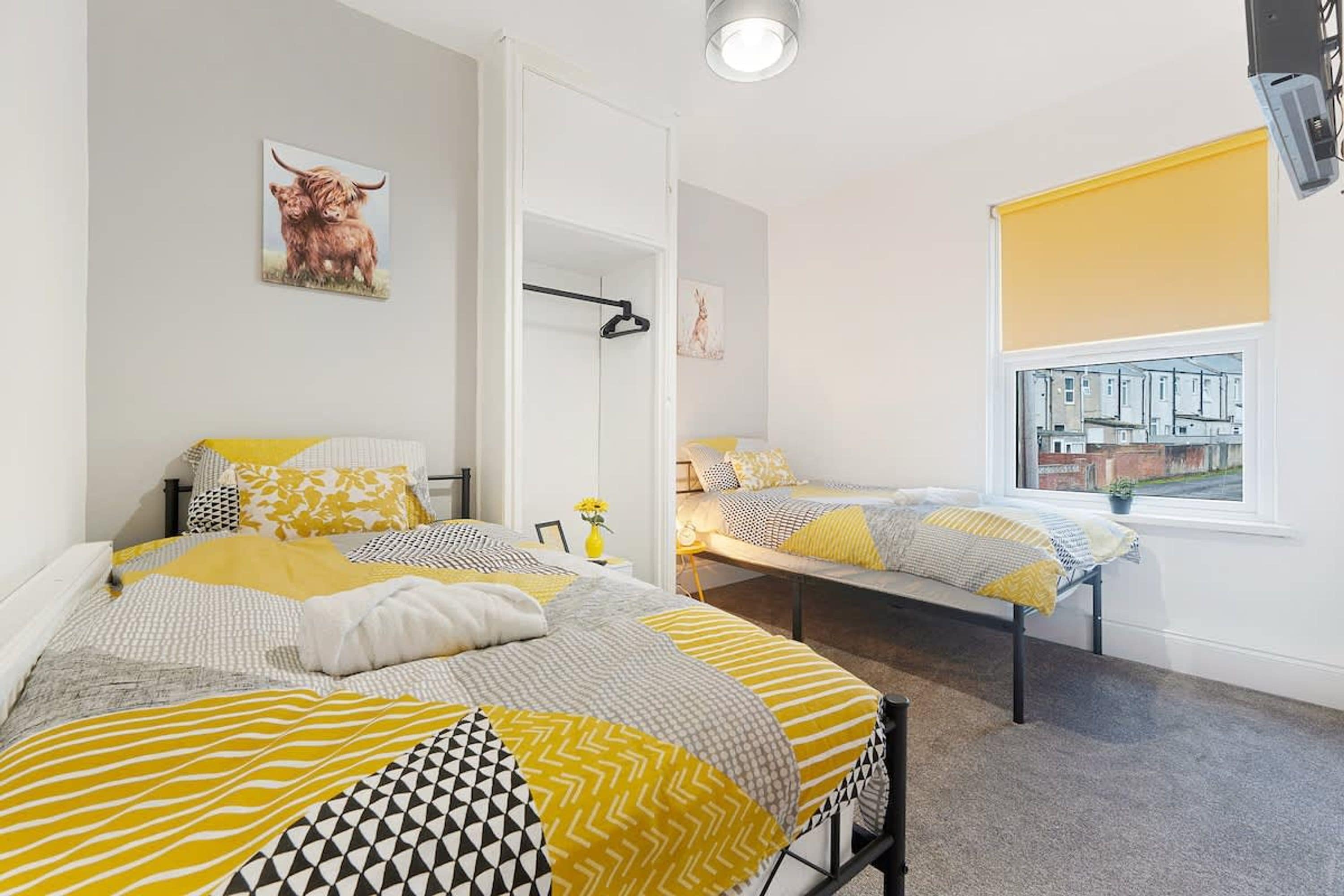 A bedroom with two beds, a window with a view of buildings, and a door leading to another room.