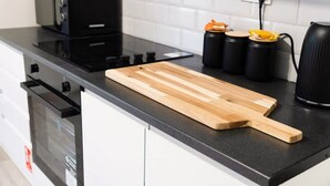 A kitchen with a black countertop, a wooden cutting board, a black kettle, and two black containers with orange lids. - Cosy 2BR Apartment Sleeps 4 by Stay With Us (Peterlee)