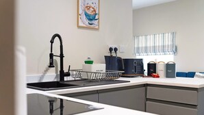 A modern kitchen with a black faucet, a sink, a coffee maker, and a window with a striped blind. - Chic Flat Steps From Barnard Castle High Street (Barnard Castle)