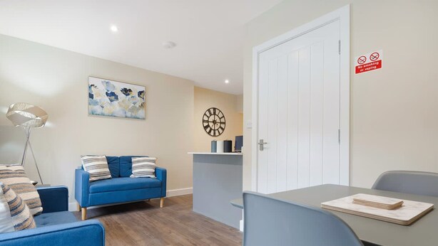 Una sala de estar moderna con un sofá azul, una mesa de comedor y un reloj en la pared.