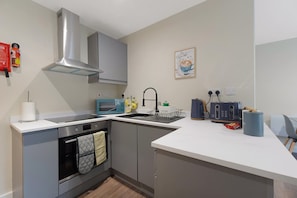 A modern kitchen with grey cabinets, a stainless steel range hood, a microwave, a sink, and a toaster. - Chic Flat Steps From Barnard Castle High Street (Barnard Castle)