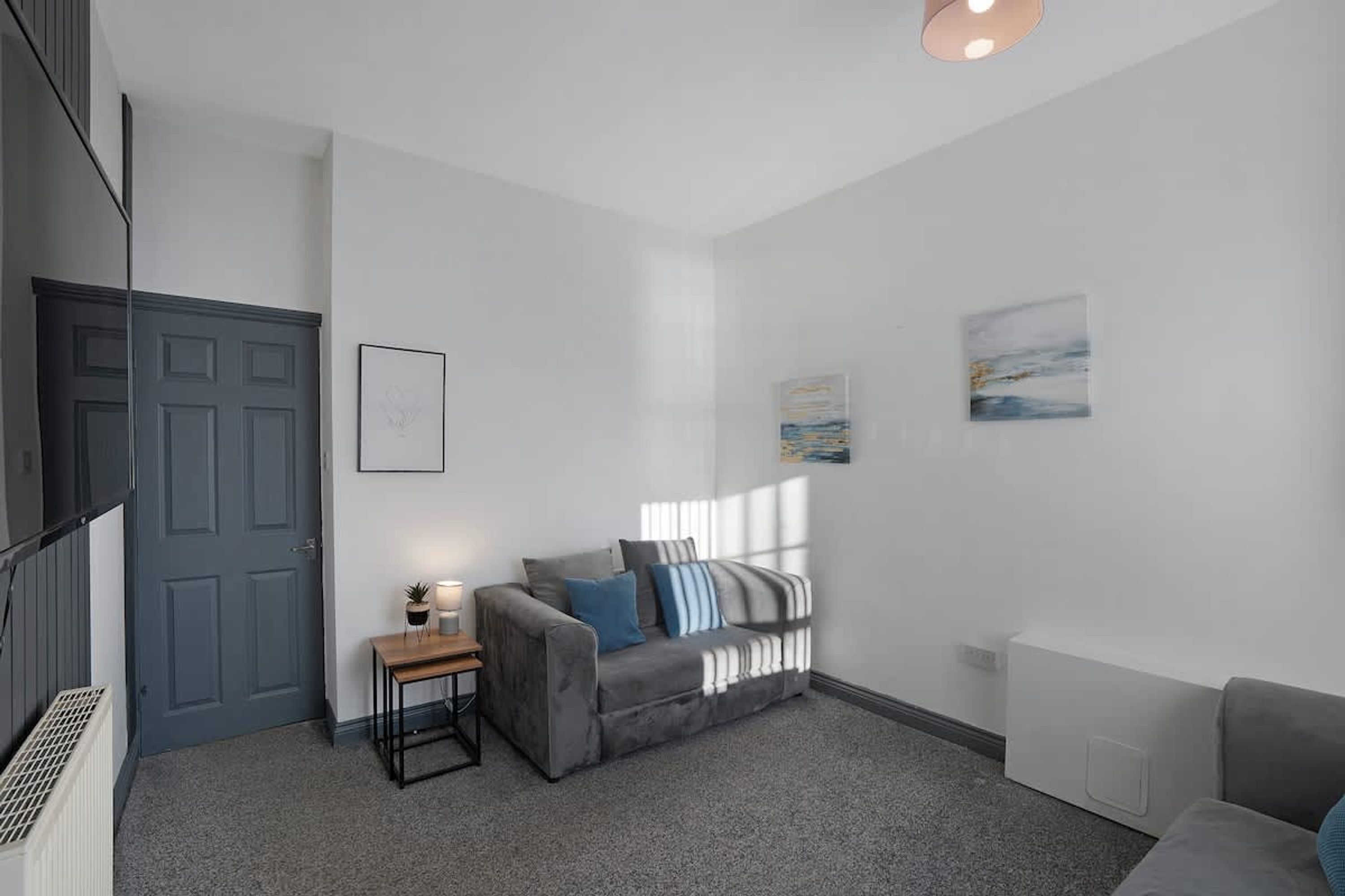 A modern living room with a grey sofa, a small side table, and a radiator.