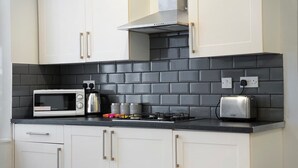 A kitchen with white cabinets, a black tiled backsplash, a microwave, a toaster, and a stove. - Stockton 5BR for Contractors With Free Parking (Stockton-on-Tees)