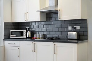 A kitchen with white cabinets, a black tiled backsplash, a microwave, a toaster, and a stove. - Stockton 5BR for Contractors With Free Parking (Stockton-on-Tees)
