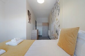 Ein Hotelzimmer mit einem Bett, einem Schminktisch, einem Heizkörper und einer Tür im Hintergrund.