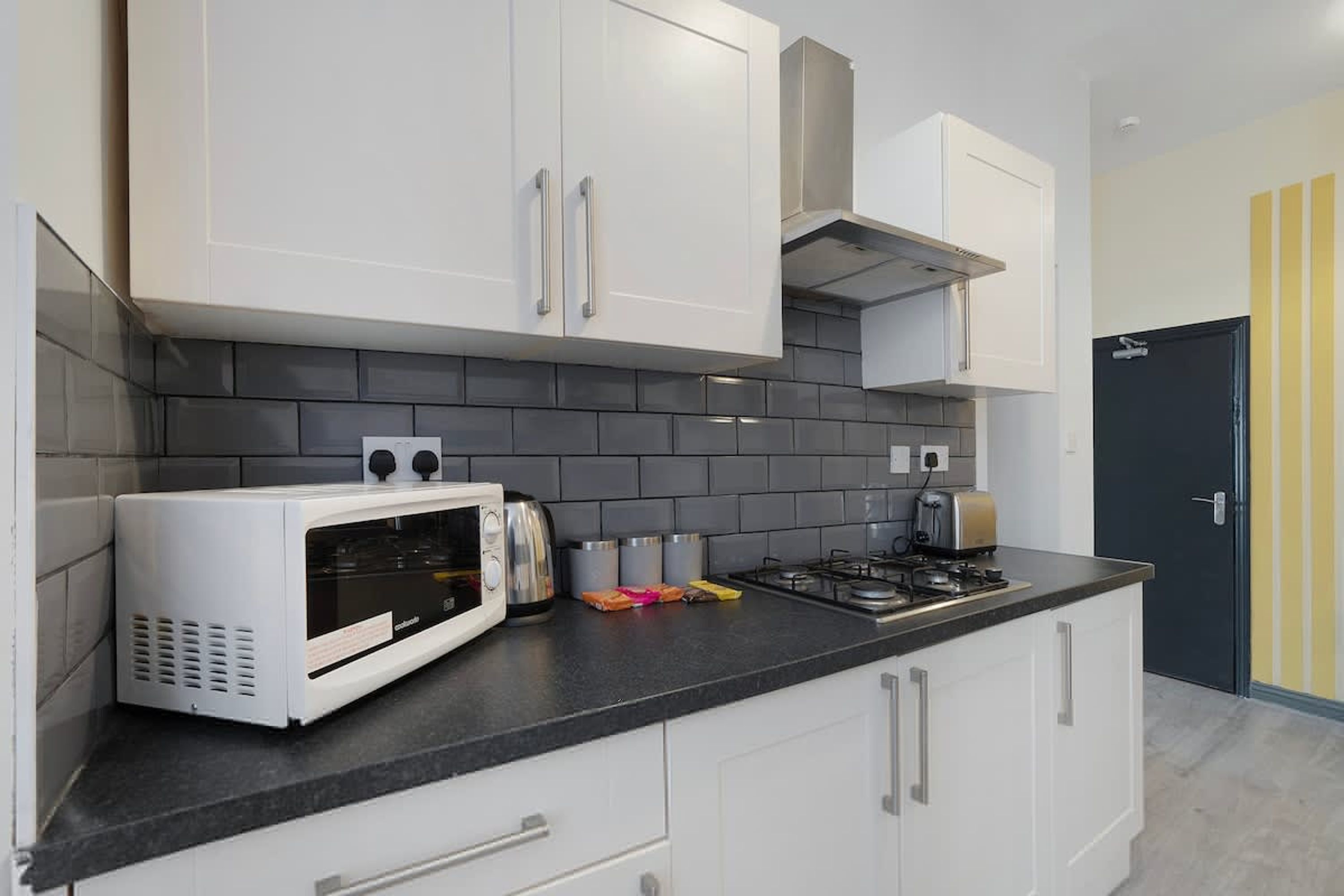 A modern kitchen with white cabinets, a black countertop, a microwave, a toaster, and a stove.