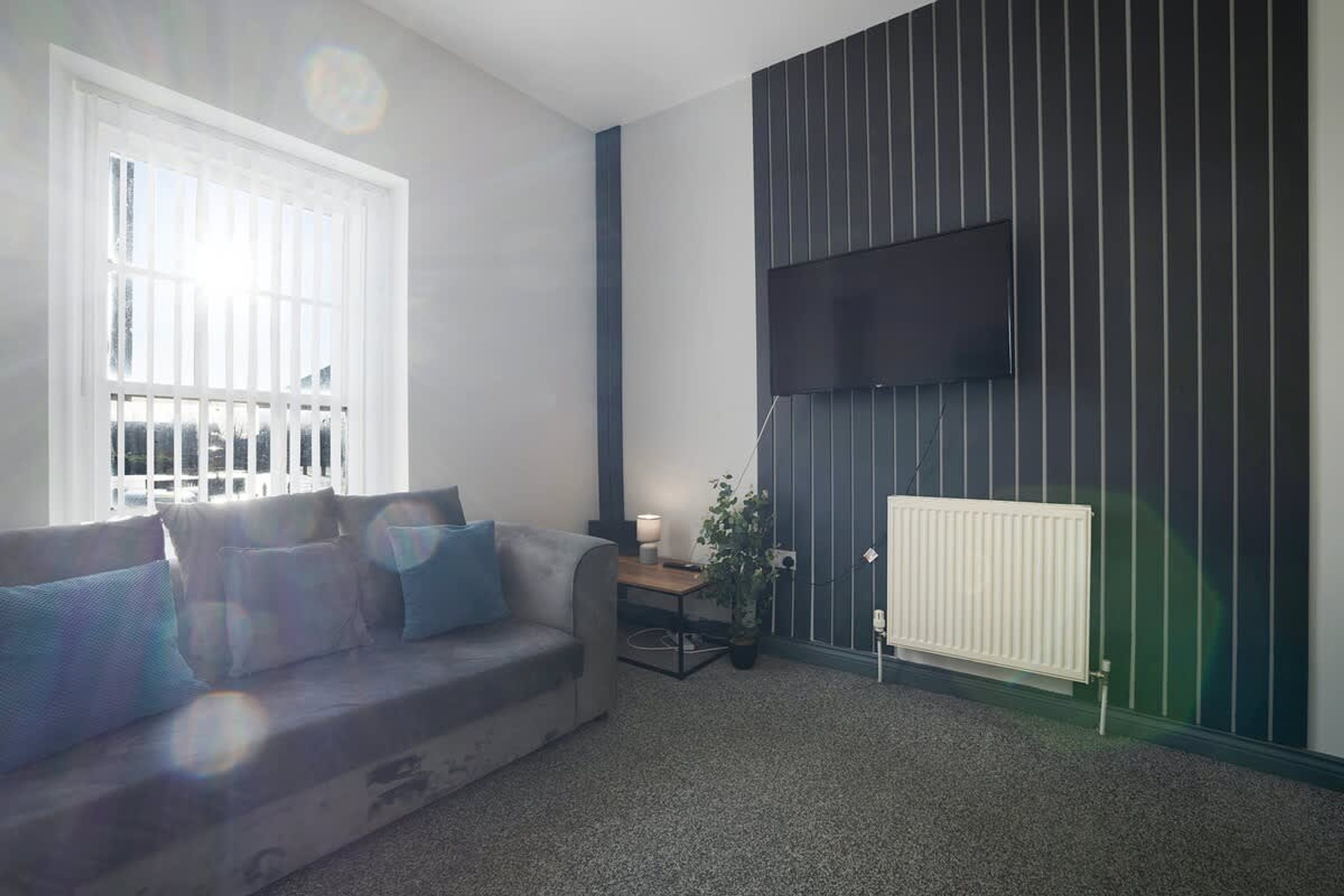 A living room with a sofa, a table, a lamp, and a radiator against a wall with vertical lines.