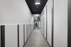 A long, narrow hallway with white walls and a grey floor, leading to a blue door at the end. - Stockton 5BR for Contractors With Free Parking (Stockton-on-Tees)