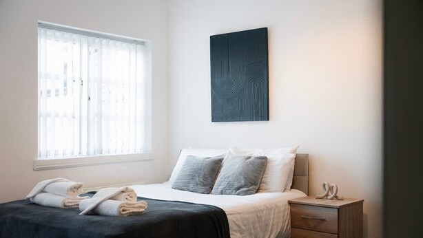A bedroom with a bed, a window, a bedside table, and a wall-mounted artwork. - Stockton 5BR for Contractors With Free Parking (Stockton-on-Tees)
