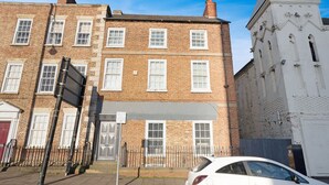 A multi-story brick building with white-framed windows, a gated entrance, and a white car parked in front. - Stockton 5BR for Contractors With Free Parking (Stockton-on-Tees)