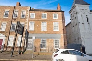 A multi-story brick building with white-framed windows, a gated entrance, and a white car parked in front. - Stockton 5BR for Contractors With Free Parking (Stockton-on-Tees)