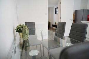 Una sala de reuniones moderna con una mesa de cristal, cuatro sillas negras y una planta de cactus.