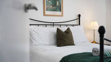 A neatly made bed with white bedding and a green throw blanket, a black metal headboard, and a framed painting above the bed.