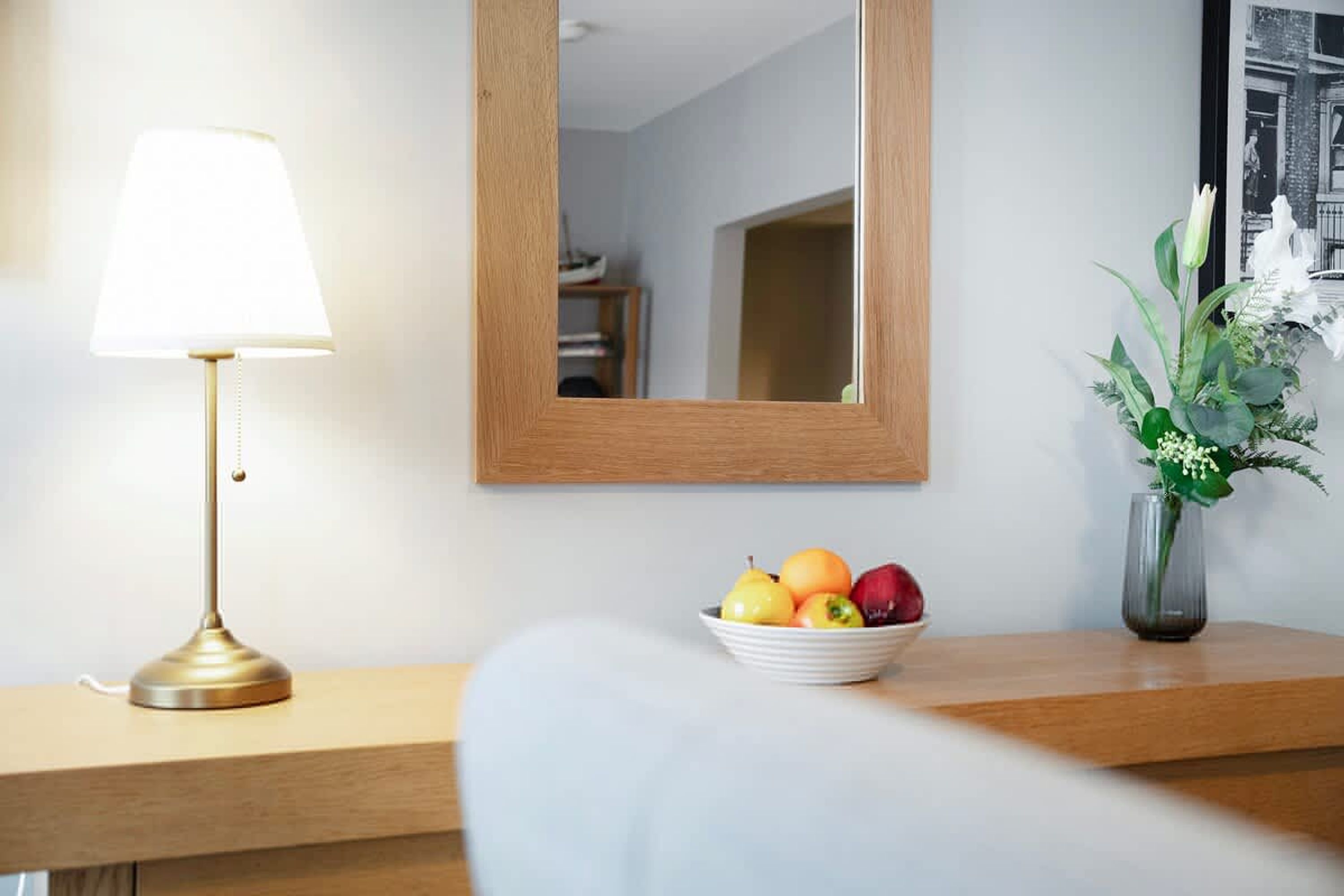 Ein Hotelzimmer mit Nachttisch, Lampe, Spiegel und Obstschale.
