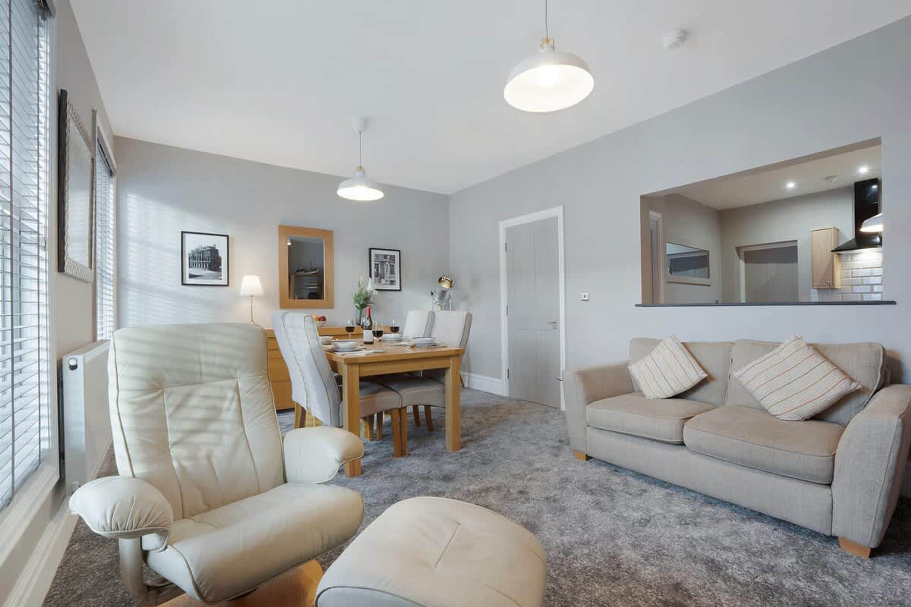 A modern living room with a sofa, armchair, dining table, and a large mirror.