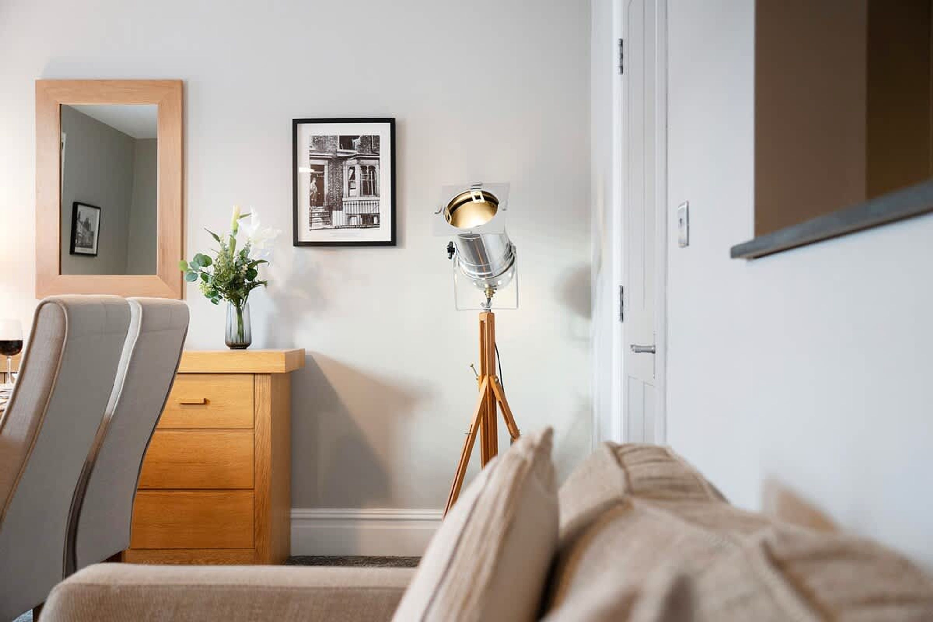 Habitación de hotel con cama, cómoda de madera, espejo, cuadro en la pared y lámpara de pie.