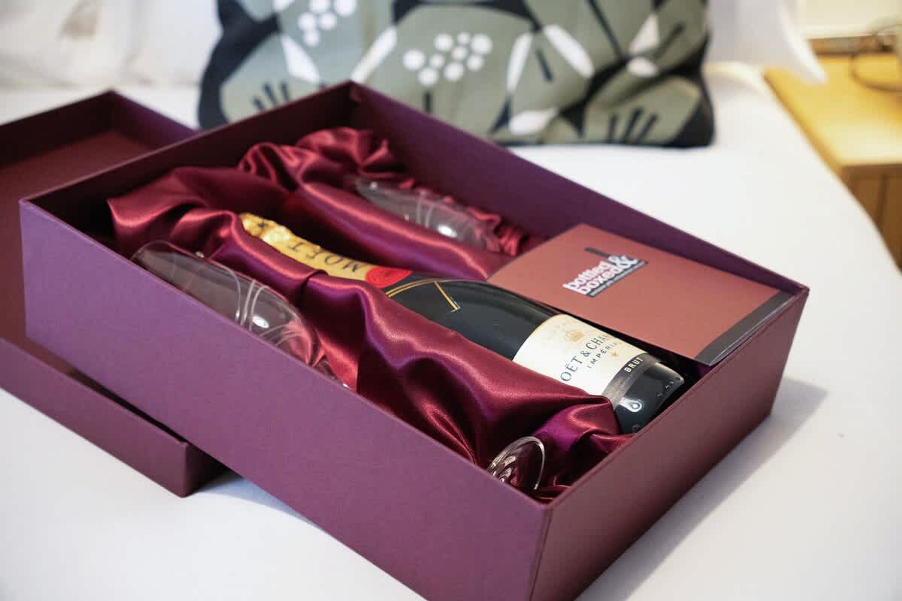 A purple box containing a bottle of wine, a glass, and a booklet.