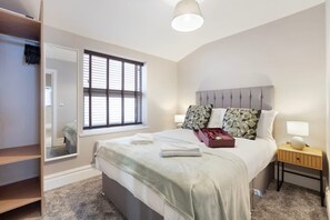 A bedroom with a bed, a nightstand, a bedside lamp, a window with blinds, a mirror, and a wardrobe. - Luxury 1 Bedroom in Hartlepool With Wifi (Hartlepool)