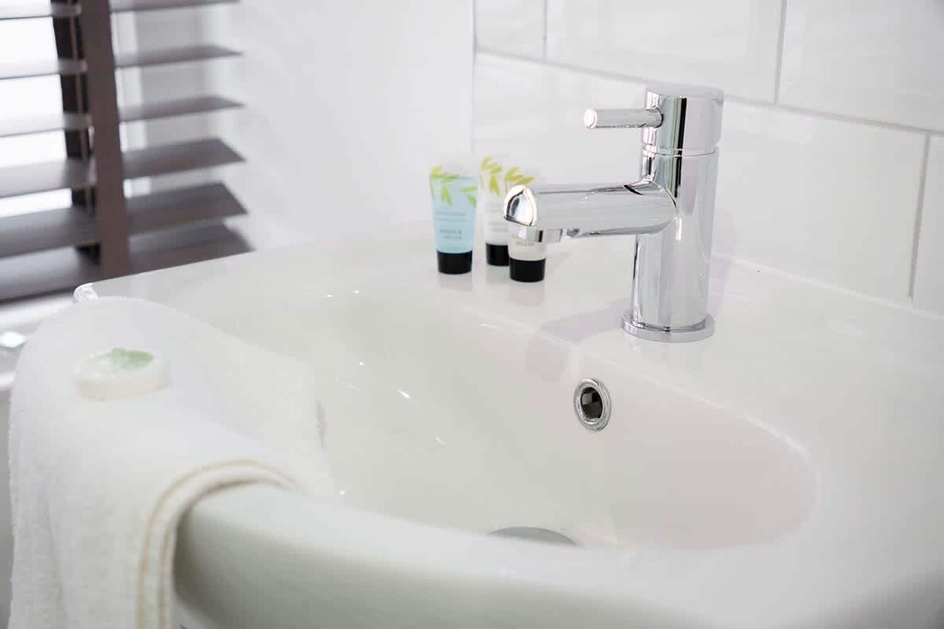 Un lavabo de salle de bain avec un robinet chromé, un porte-savon et deux flacons de produits de toilette.