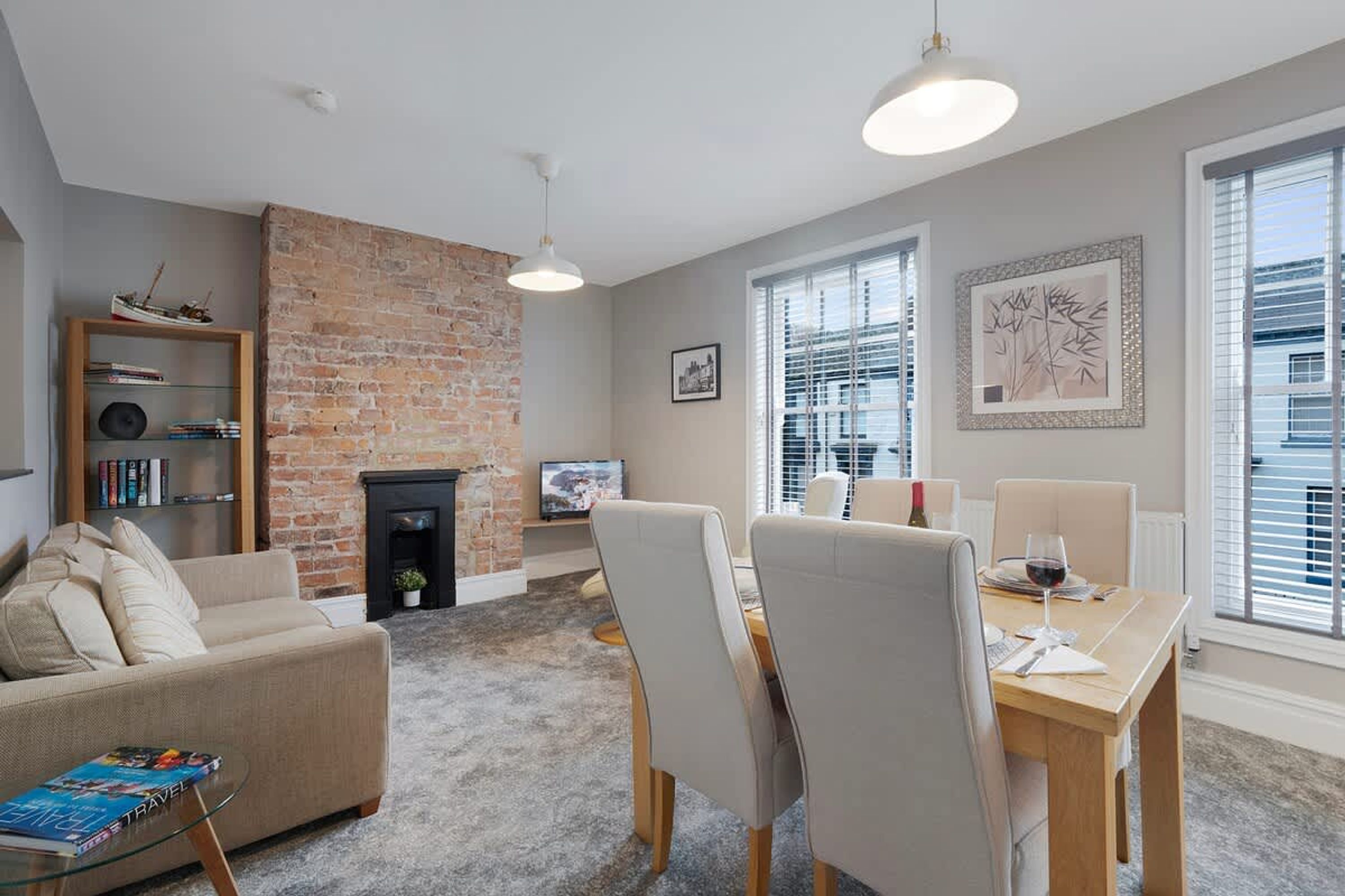 A living room with a brick fireplace, a sofa, a dining table with chairs, and a bookshelf.