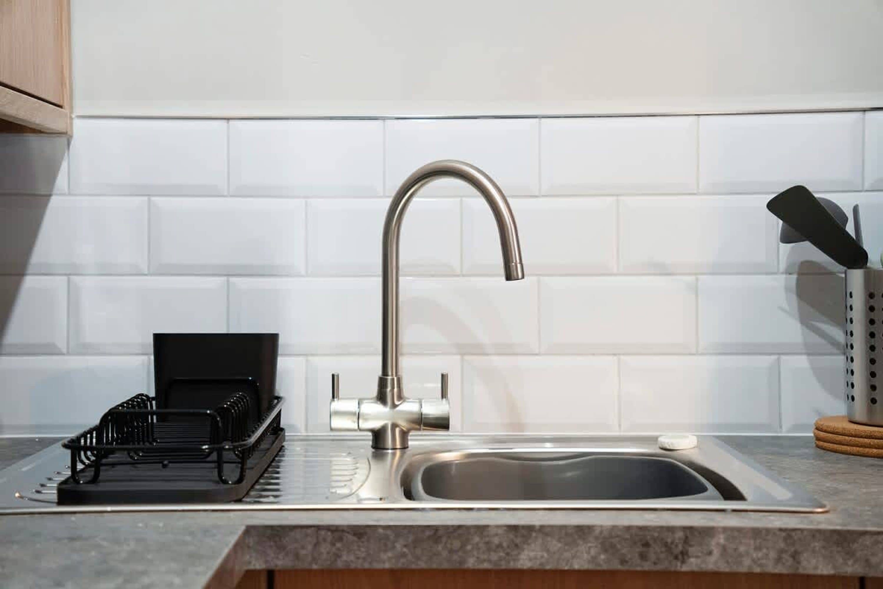 A kitchen with a stainless steel sink, a black dish rack, and a knife block.