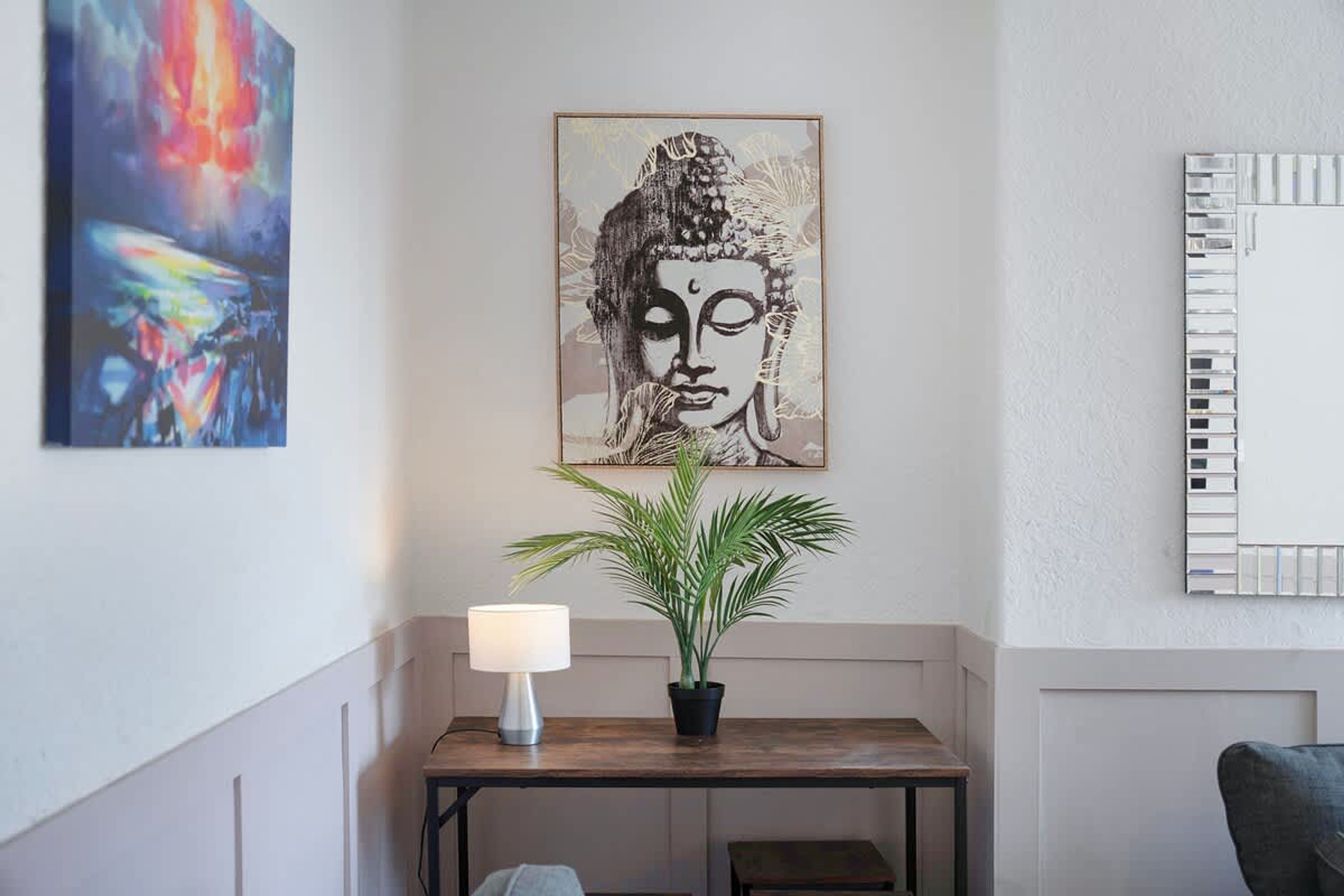 A room with a Buddha painting, a potted plant, a lamp, and a mirror on the wall.