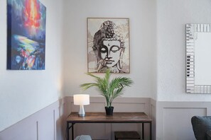 Een kamer met een boeddhaprent, een plant in pot, een lamp en een spiegel aan de muur.