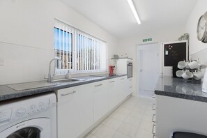 A modern kitchen with a built-in washing machine, a sink, and a window with blinds. - Stylish 3BR Stay Sleeps 9 by Stay With Us (Trimdon Station)