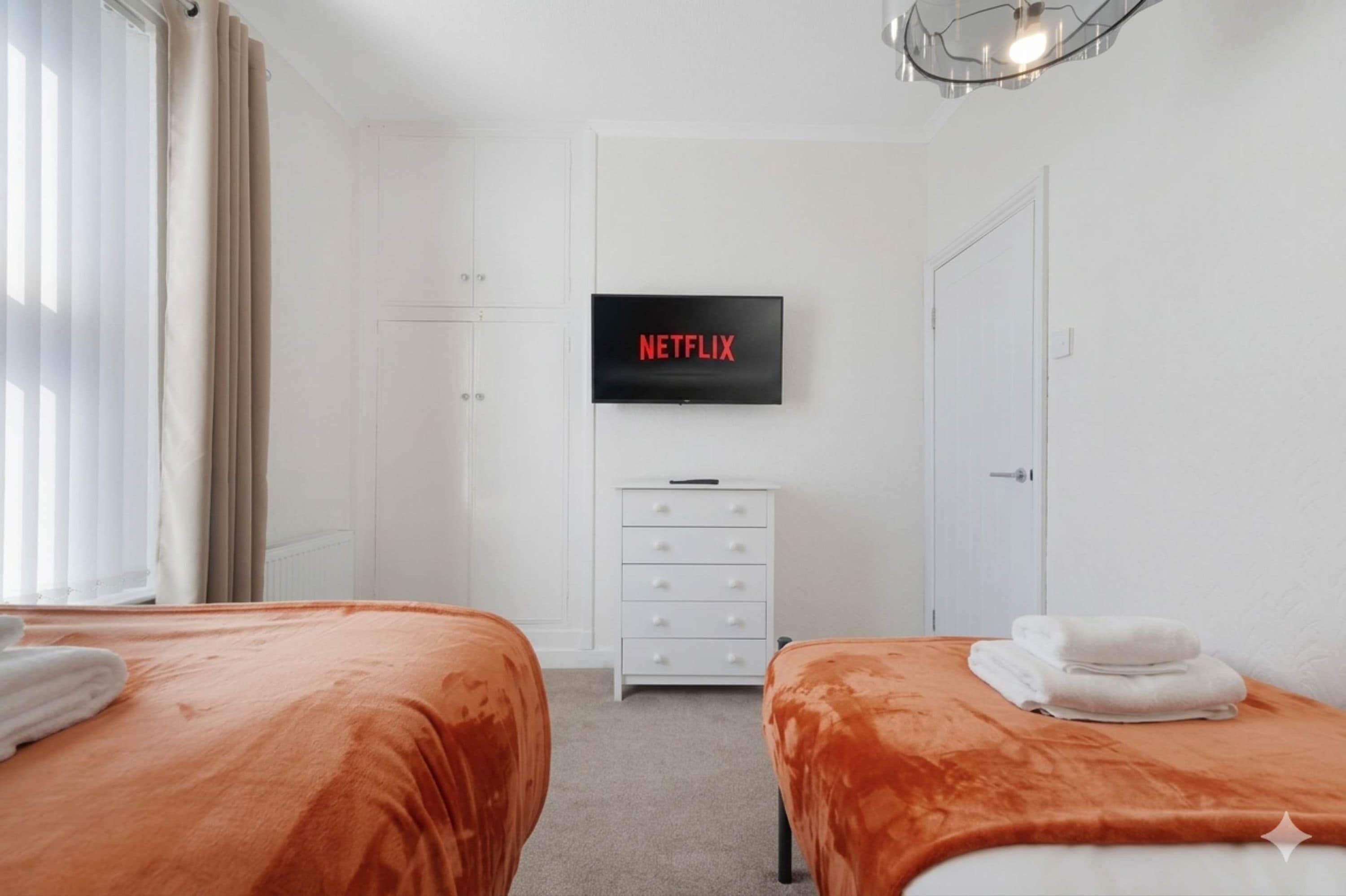 Une chambre d’hôtel avec deux lits, un téléviseur fixé au mur, une commode blanche et une porte.