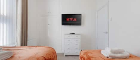 A hotel room with two beds, a TV mounted on the wall, a white dresser, and a door.