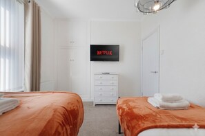 A hotel room with two beds, a TV mounted on the wall, a white dresser, and a door. - Stylish 3BR Stay Sleeps 9 by Stay With Us (Trimdon Station)