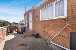 A residential property with a brick exterior, a front door, a small set of steps leading to the entrance, and a visible trash bin. - Stylish 3BR Stay Sleeps 9 by Stay With Us (Trimdon Station)