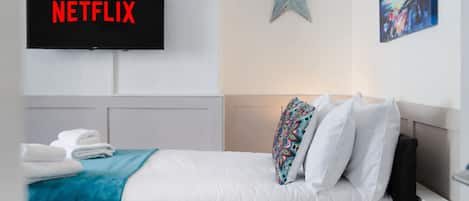 A hotel room with a bed, a TV mounted on the wall displaying 'NETFLIX', a star decoration, and a painting on the wall.